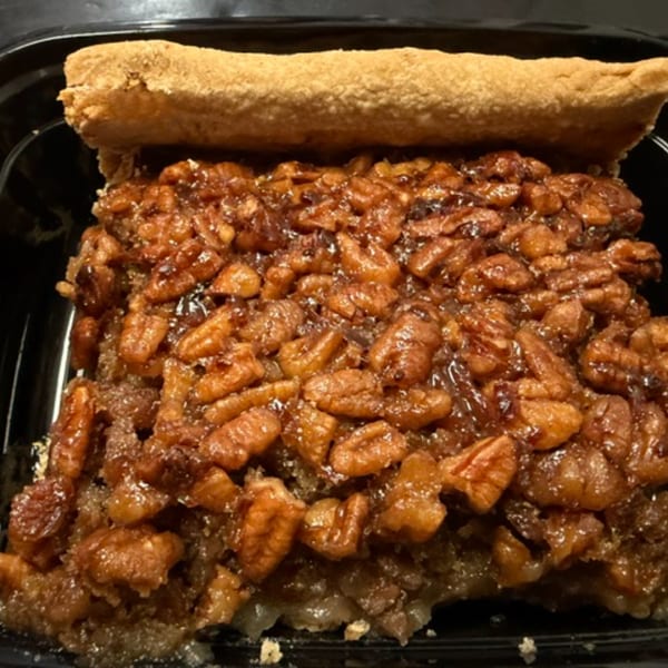 A close-up of a pecan pie slice with a golden crust and glistening pecan topping.
