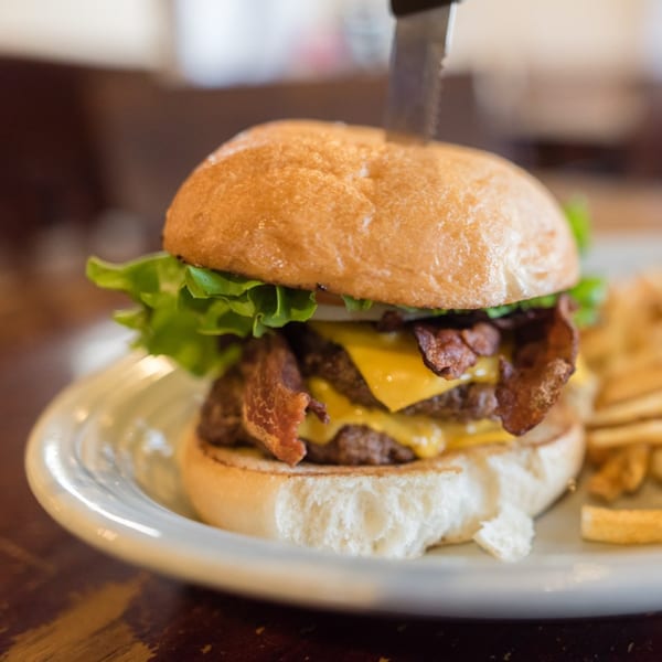 A double cheeseburger with bacon, lettuce, and a knife through the bun, served with fries.