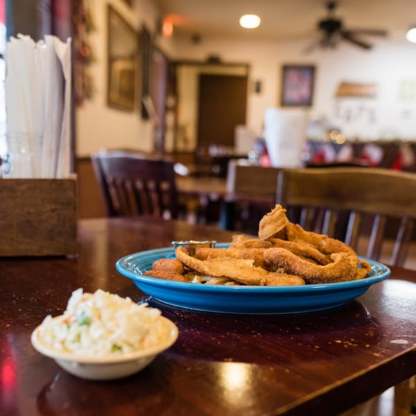 Fried fish and hush puppies on a blue plate with coleslaw on a wooden table in a restaurant.