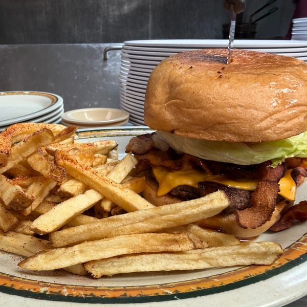A large burger with cheese, bacon, and lettuce, served with a pile of seasoned fries.