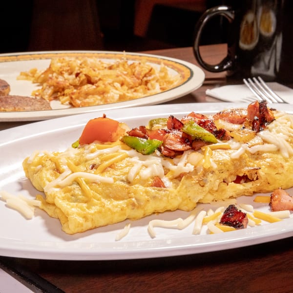 A fluffy omelet topped with melted cheese, diced tomatoes, green peppers, and bacon bits.