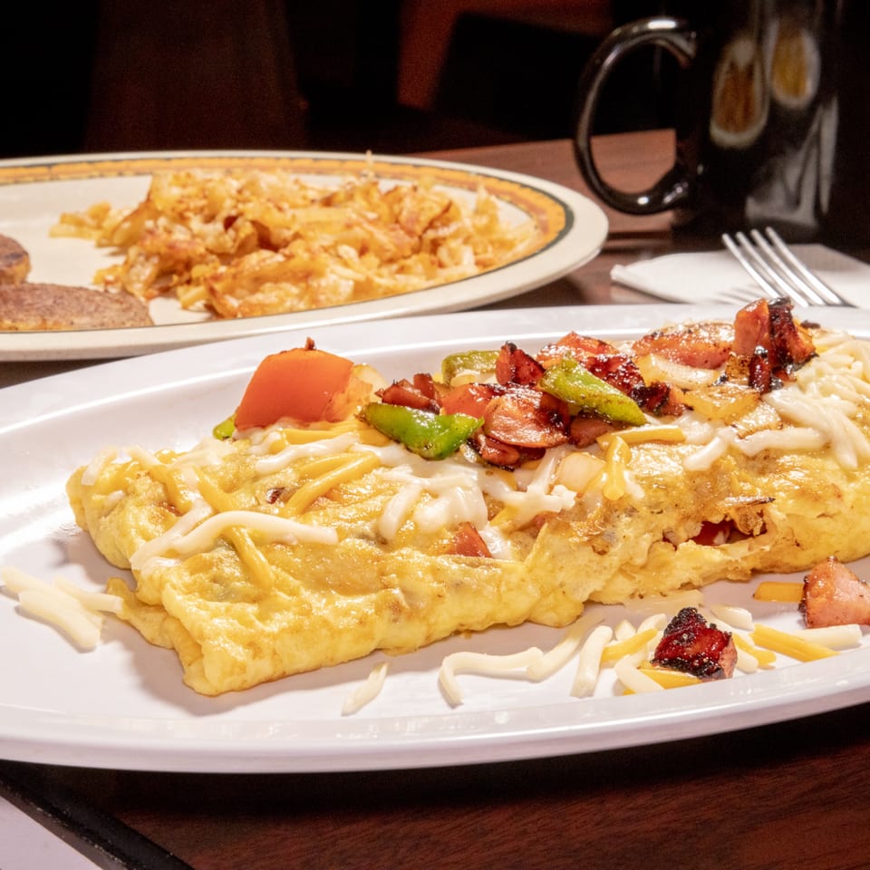 A fluffy omelet topped with melted cheese, diced tomatoes, green peppers, and bacon bits.