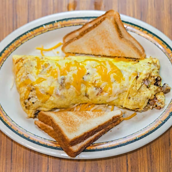 A cheese omelet with shredded cheese and two pieces of toast on a white plate.
