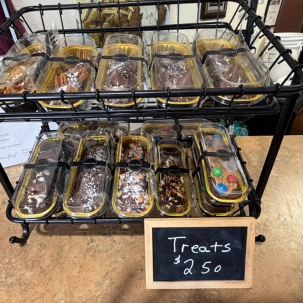 Packaged dessert treats, including brownies and cookies, displayed on a black metal rack with a "Treats $2.50" sign.
