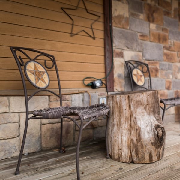 Wrought iron chairs with star-patterned backs and a tree stump table on a rustic porch.