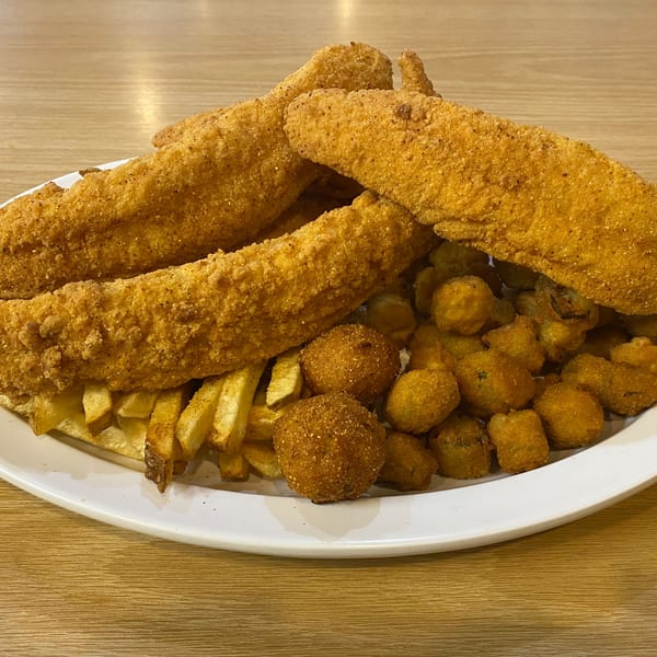 A plate of fried fish, french fries, hush puppies, and fried okra on a wooden table.