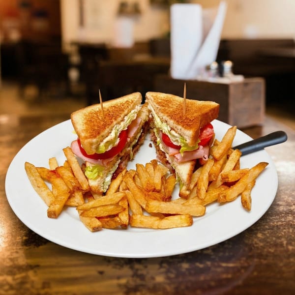A club sandwich, cut in half and held together with toothpicks, served with a side of golden fries.