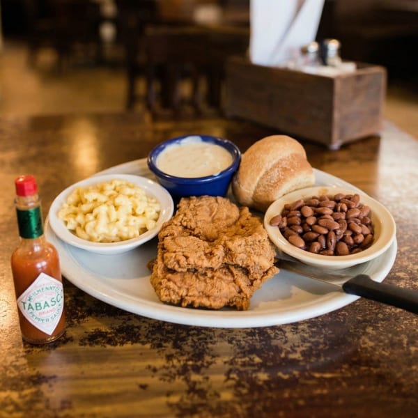 Fried chicken, mac and cheese, beans, a roll, and gravy on a white plate with Tabasco.