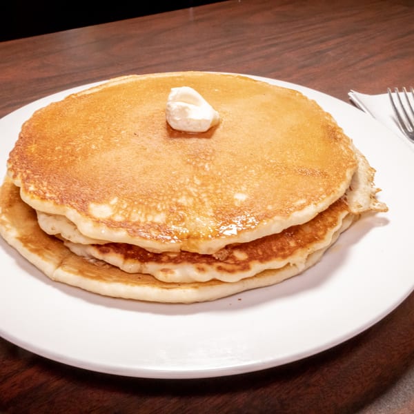 Stack of golden pancakes with melting butter and syrup on a white plate.